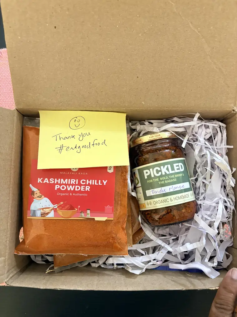 A Malayali Kada gift box packed with chilli powder and a pickle jar, with a handwritten note