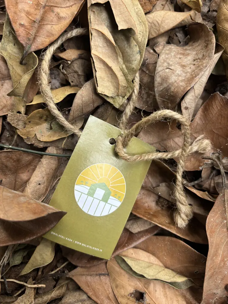 A Malayali Kada kraft tag tied with twine, resting on dry leaves